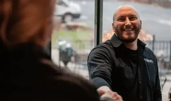Smiling man in a black jacket shaking hands across a windowed café table