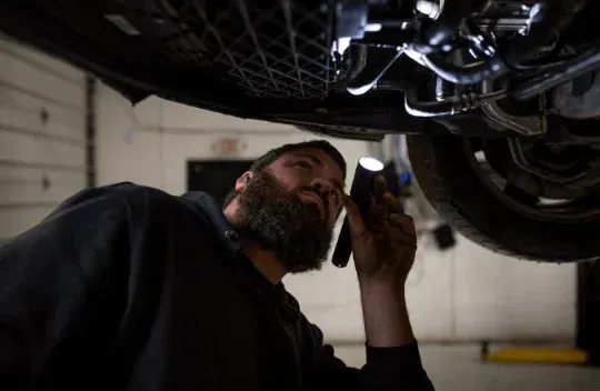 Mechanic inspecting the underside of a car in a garage with a flashlight
