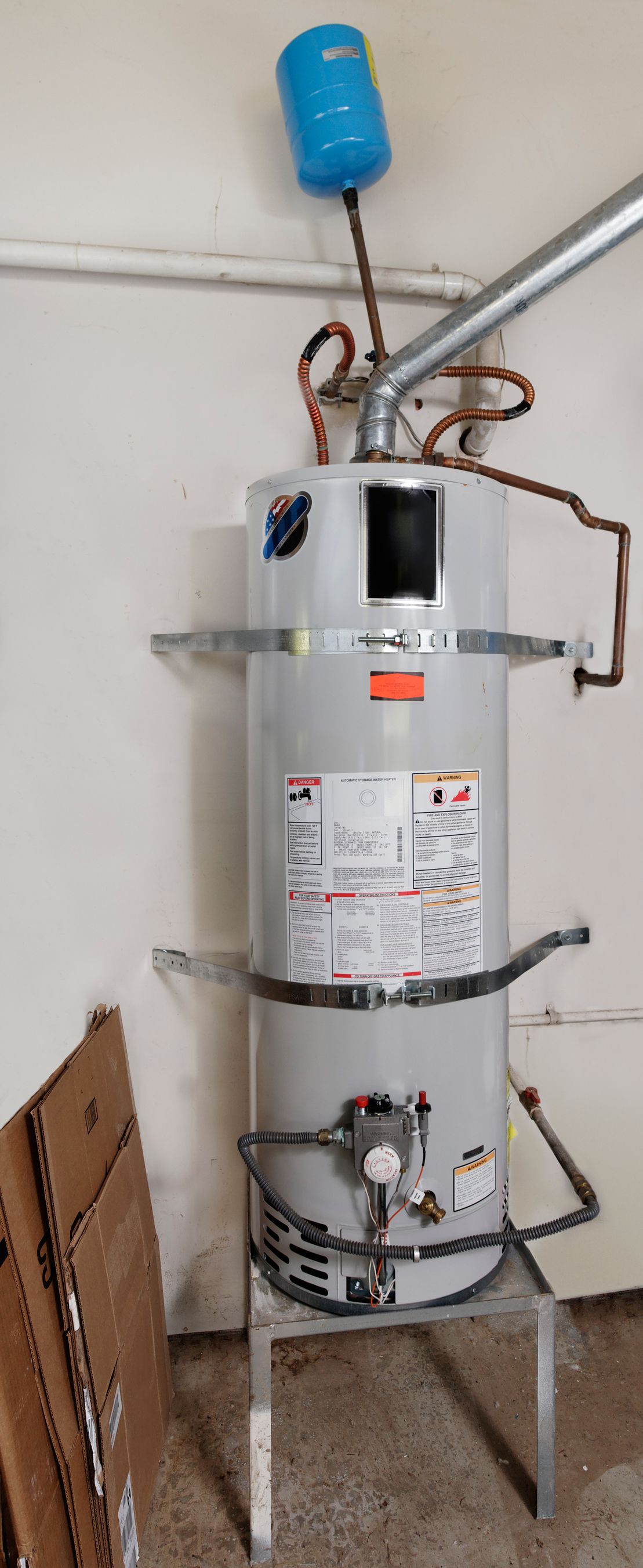 A white water heater is hanging from the ceiling in a bathroom.