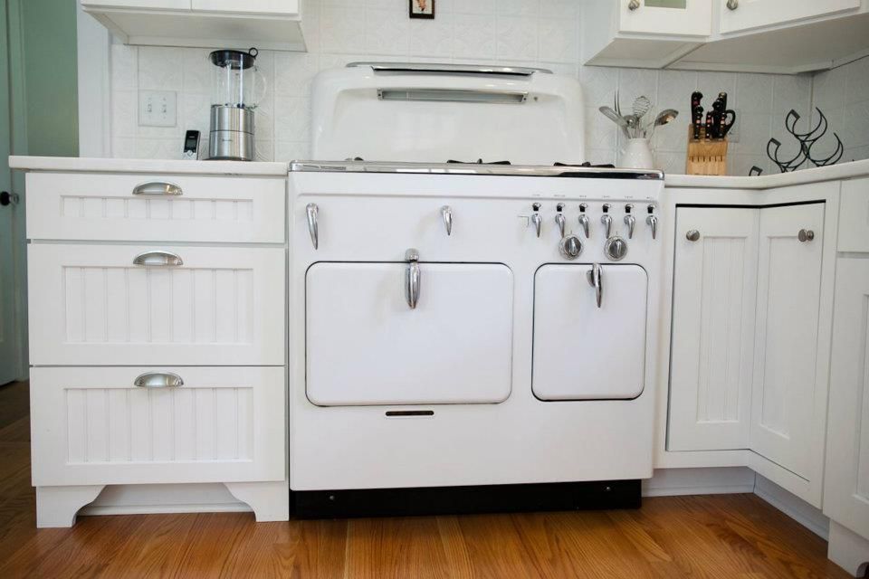 White vintage stove and cabinets in a kitchen with wooden floors.