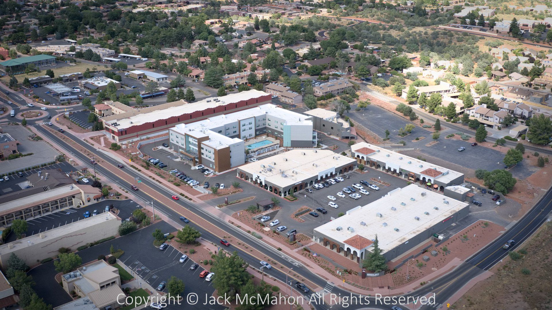 Aerial view of buildings, roads, and parking lots in a desert-like environment with trees.