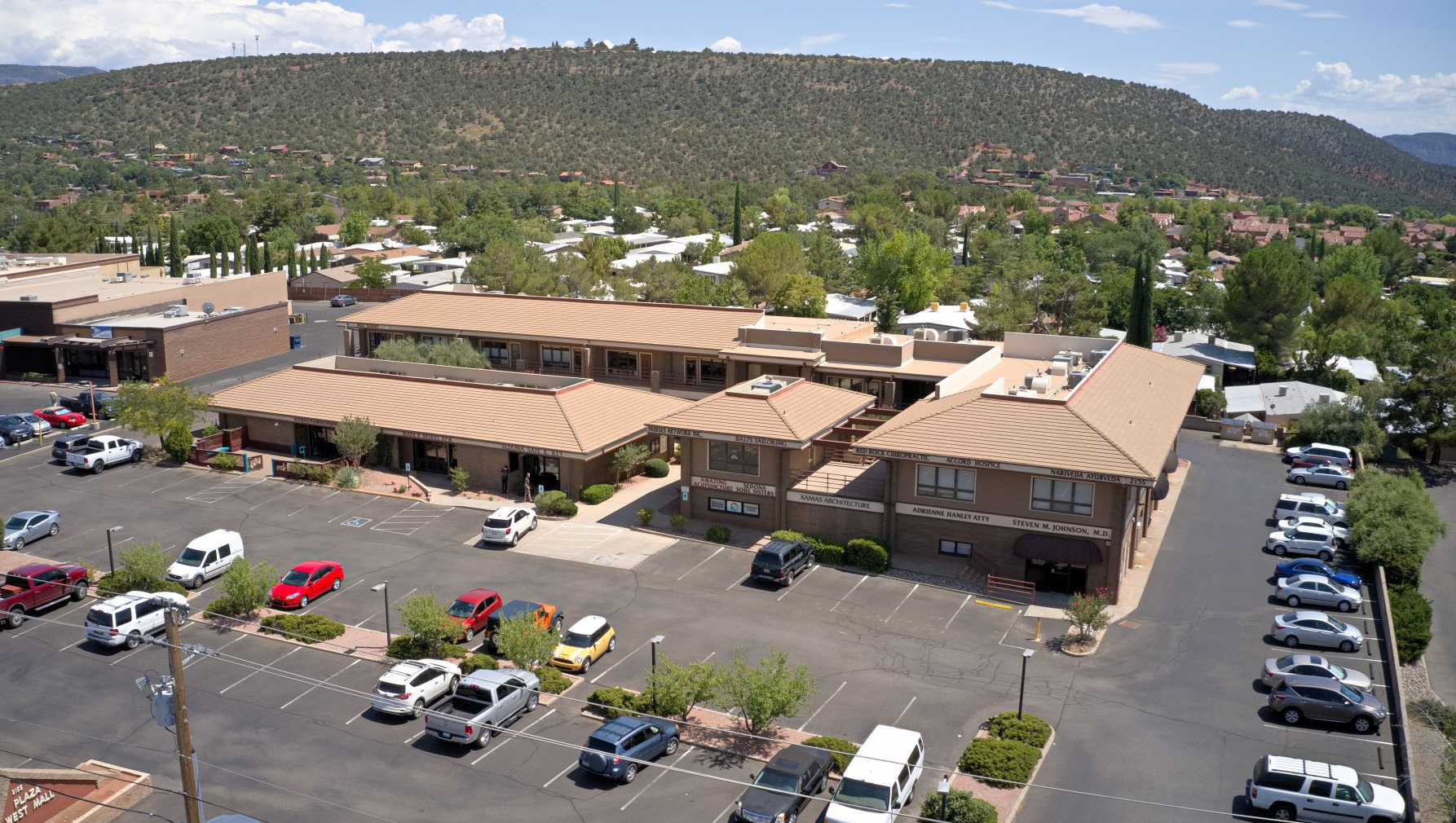 Office buildings with brown roofs and parking lot, trees and mountain backdrop.
