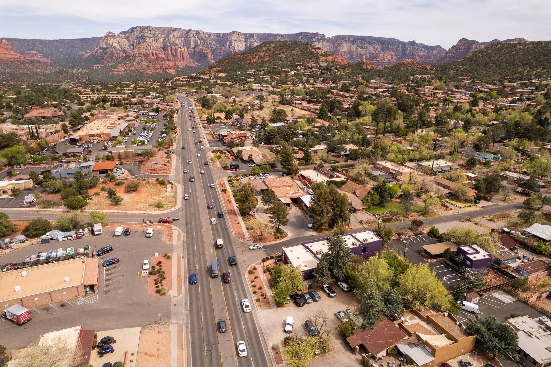 Aerial view of a town with a highway running through it, surrounded by red rock mountains and green vegetation.
