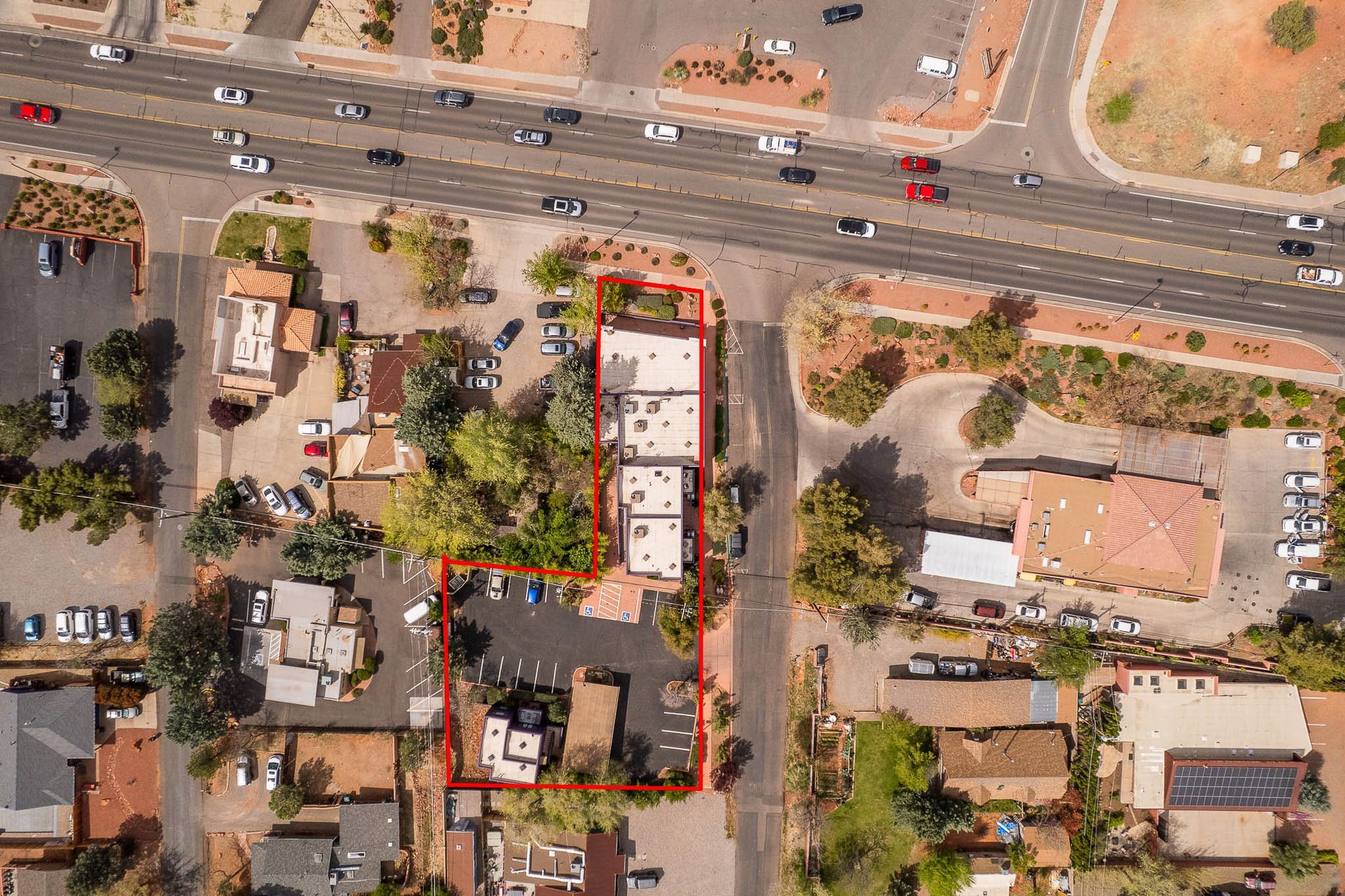 Aerial view of buildings, roads, and parking areas in a town; outlined in red.