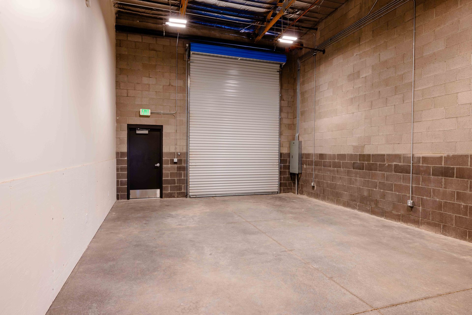 Empty warehouse interior with a large roll-up door, side door, and concrete floor.