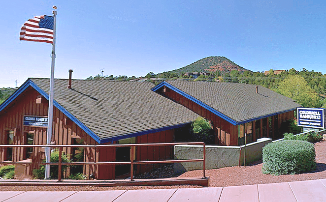 Brown building with blue trim, an American flag, and a mountain in the background.