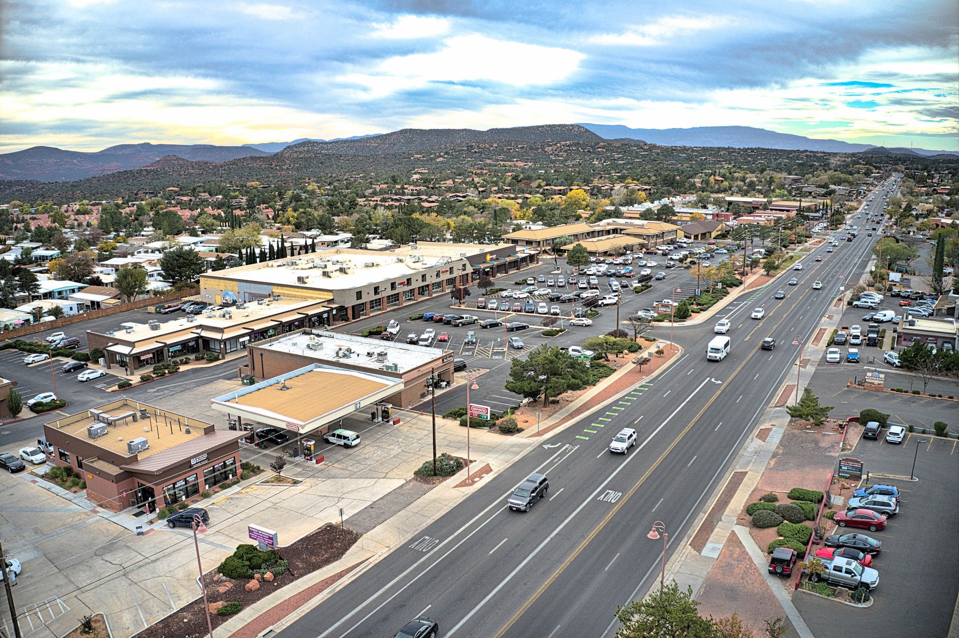 Aerial view of a town with a multilane road, buildings, parking lots, and a mountain backdrop.