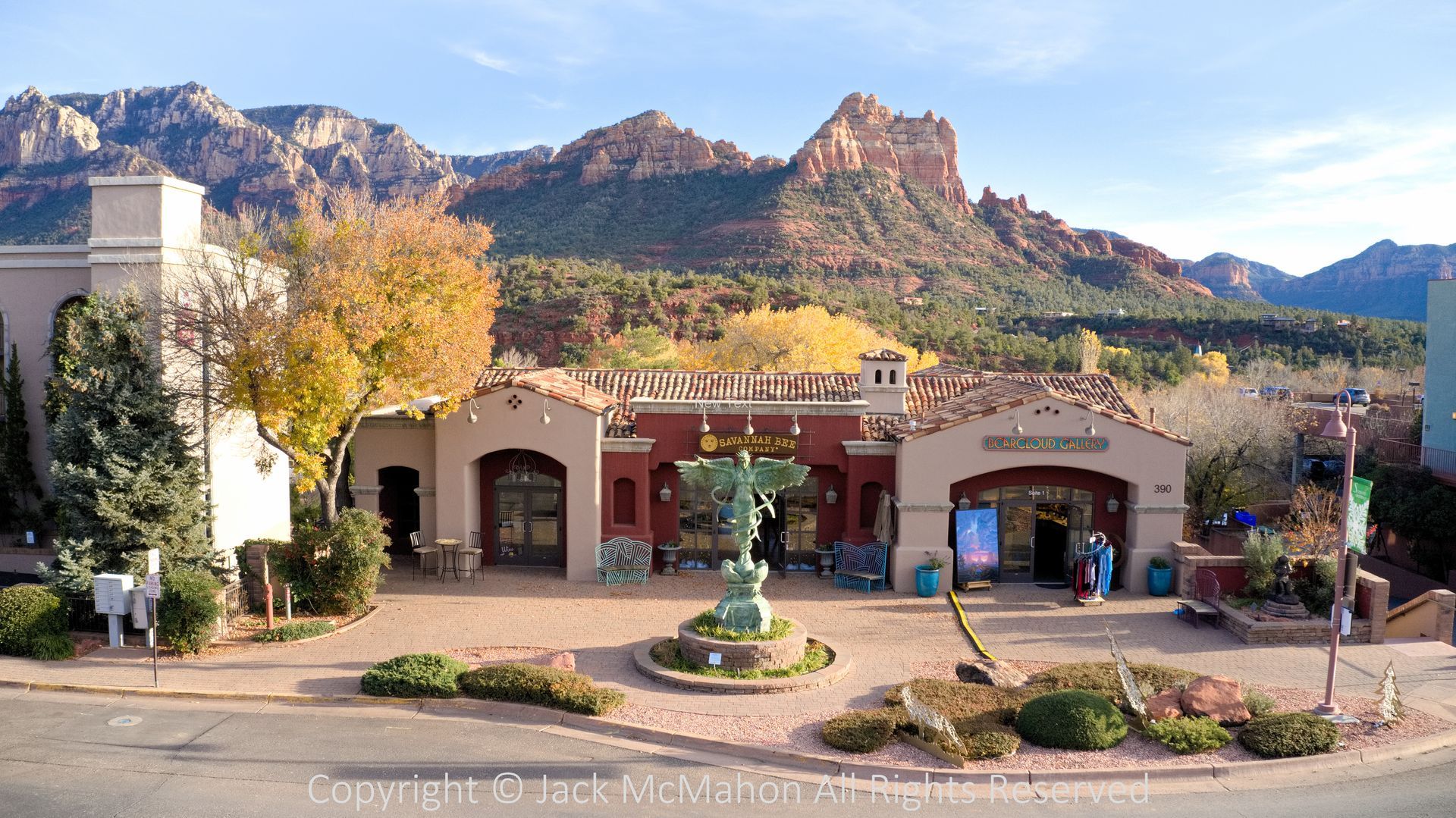 Shops with red tile roofs and angel statue in Sedona, Arizona, with red rock mountains in the background.