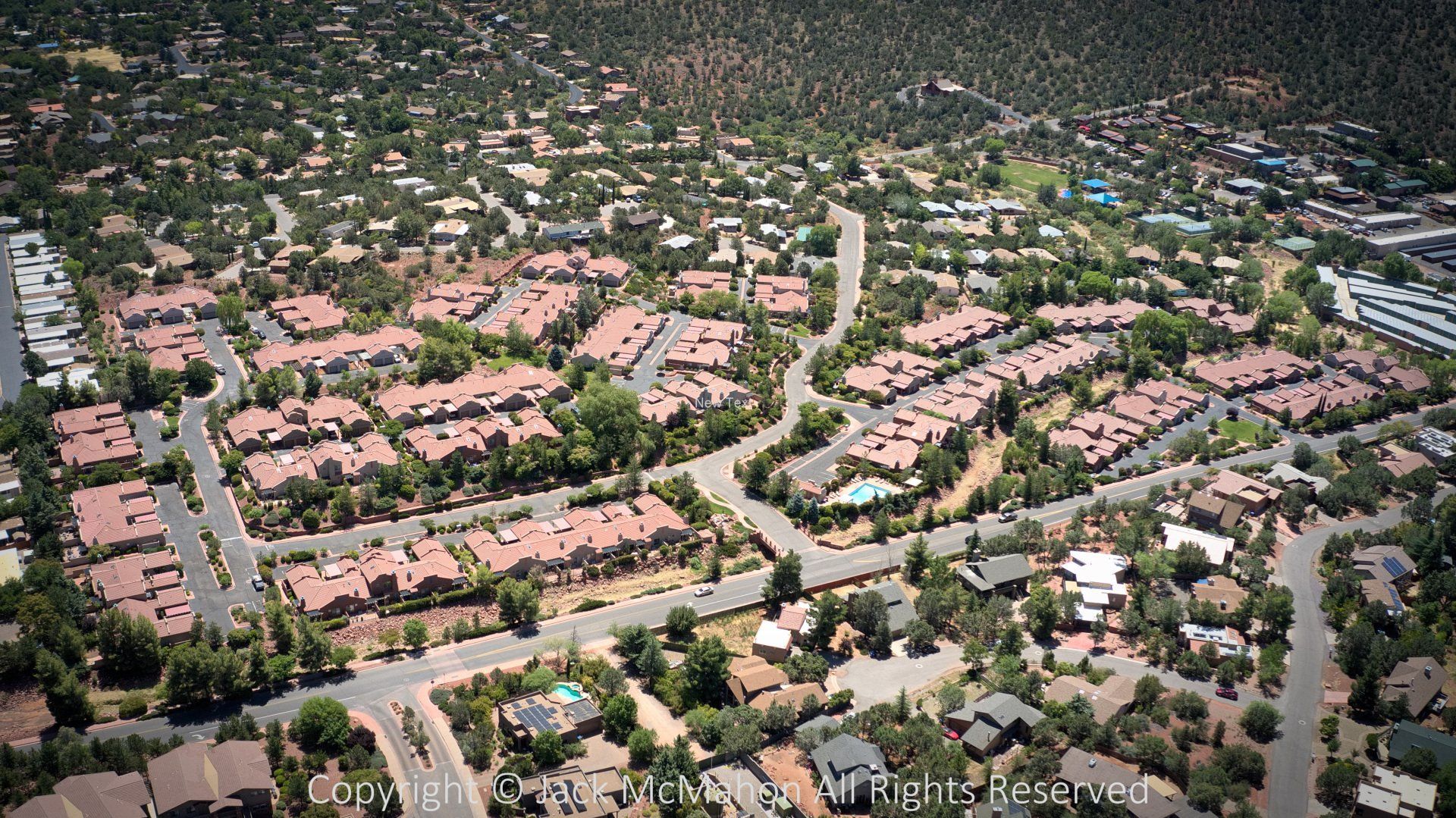 Aerial view of a residential neighborhood with red-roofed buildings surrounded by trees and roads.