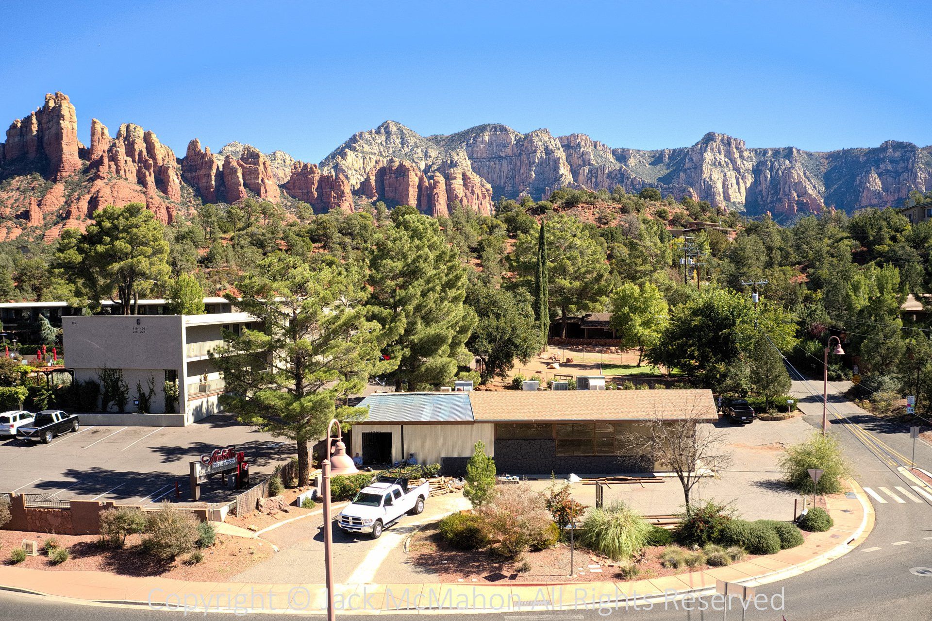 Sedona, Arizona landscape with red rock formations behind buildings and trees. Bright, sunny day.