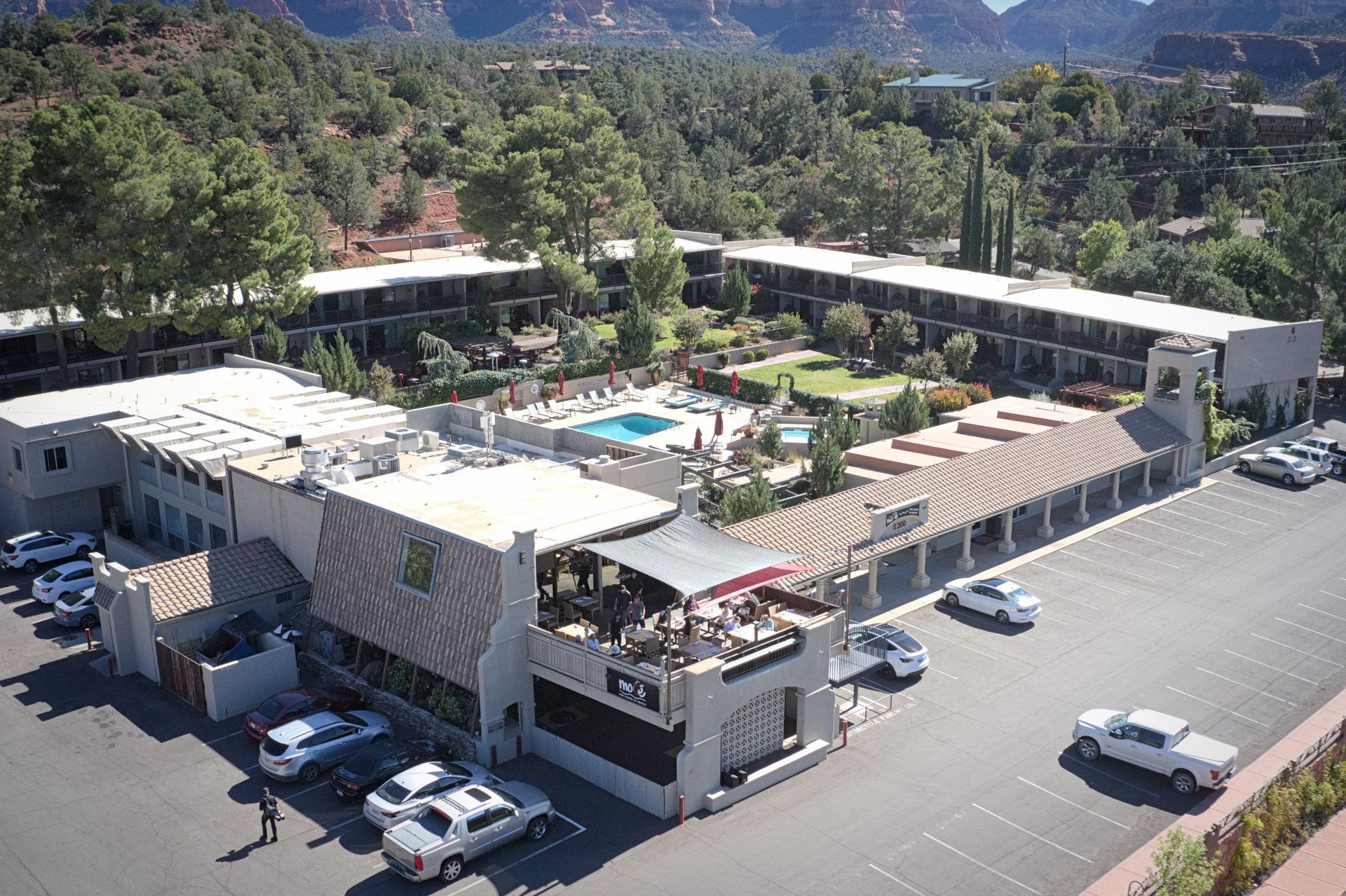 Hotel complex with pool, patio, parking, and surrounding red rock mountains.