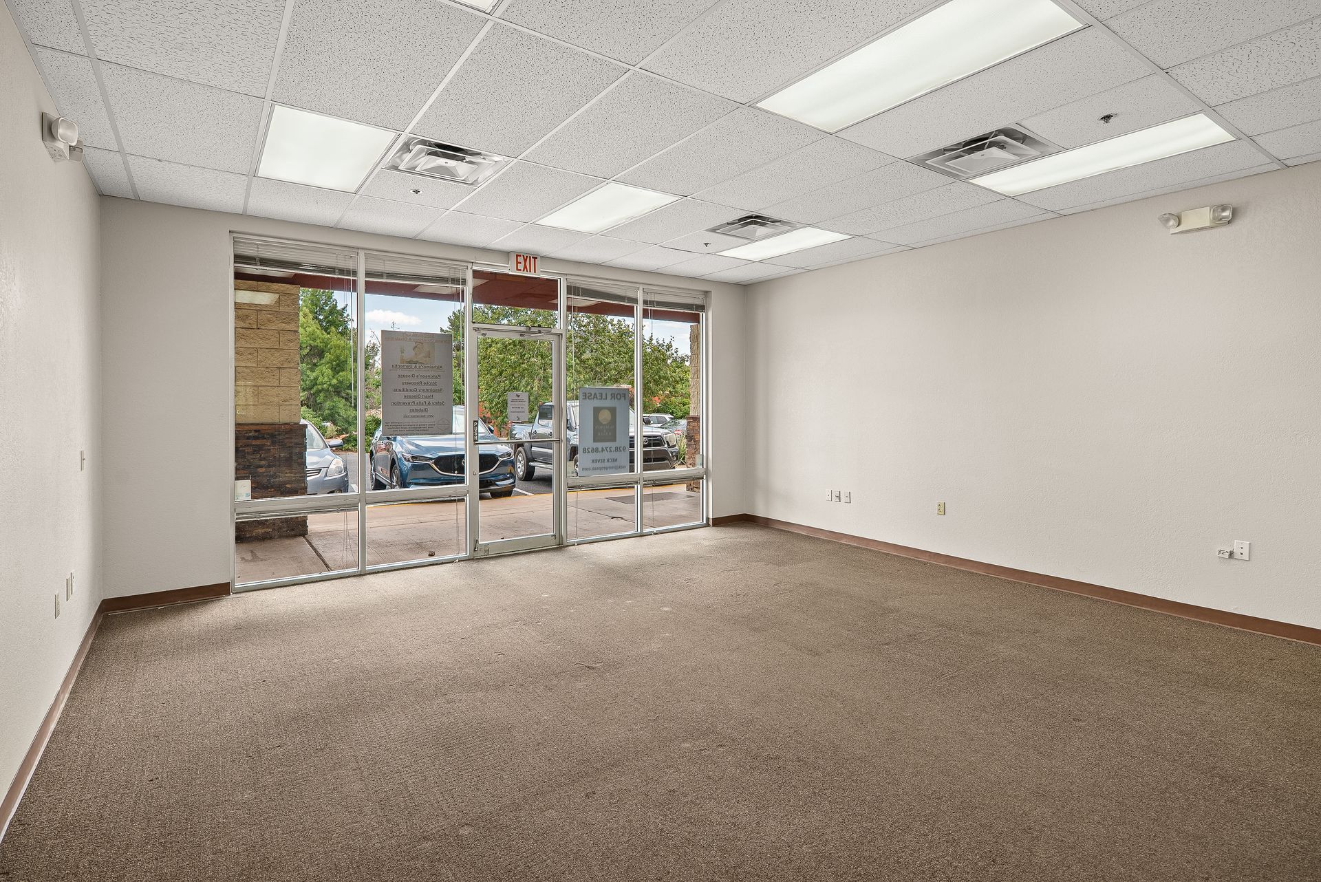 Empty commercial space with large front windows, carpet, and ceiling lights.
