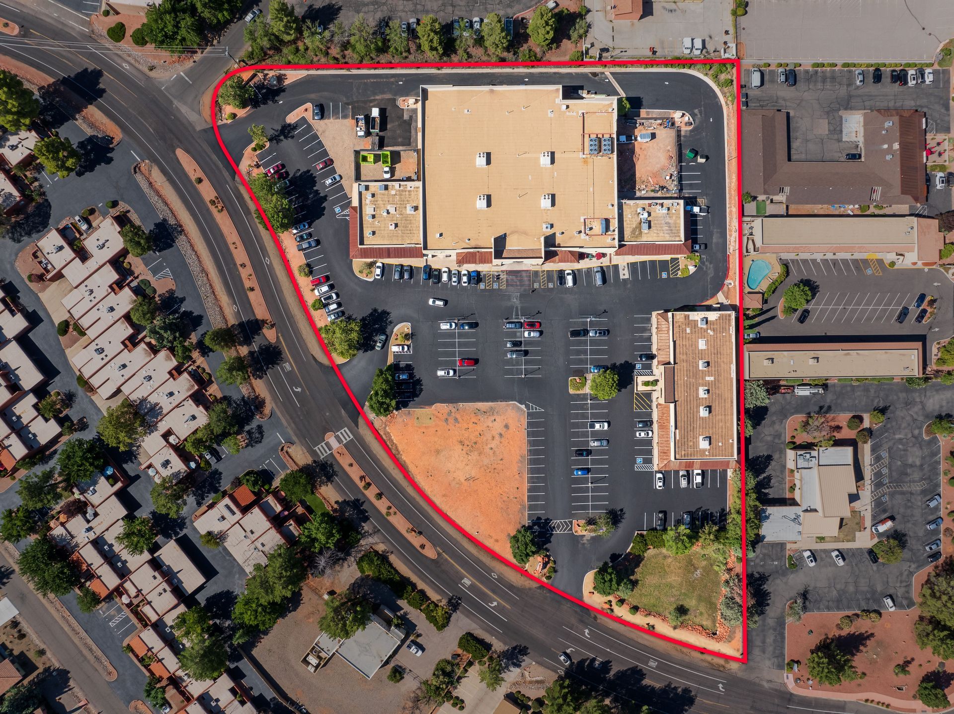 Aerial view of a commercial complex, outlined in red, with buildings, parking, and roads in a desert environment.