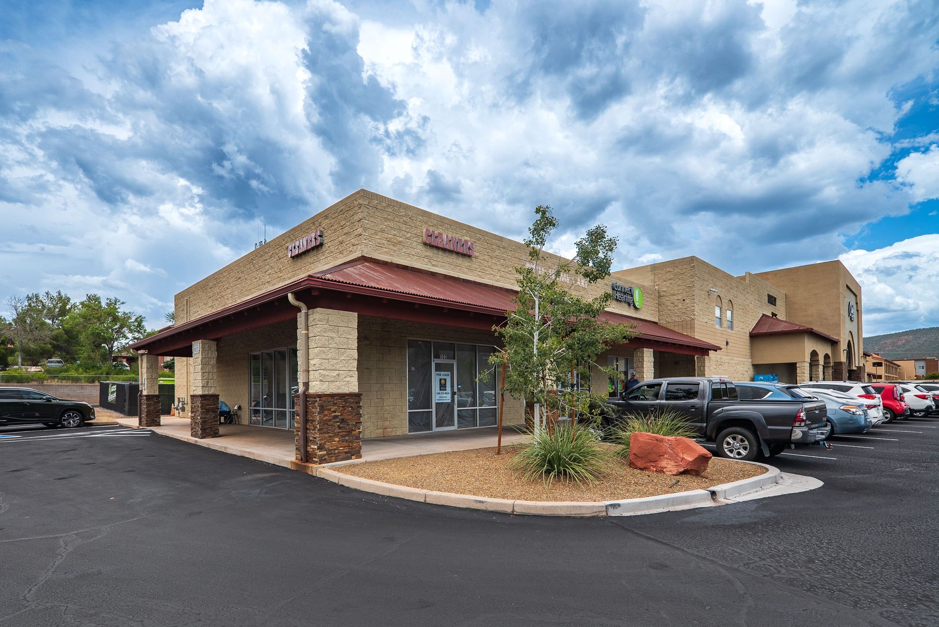 Tan building with red tile roof, cars parked in front. Cloudy sky.