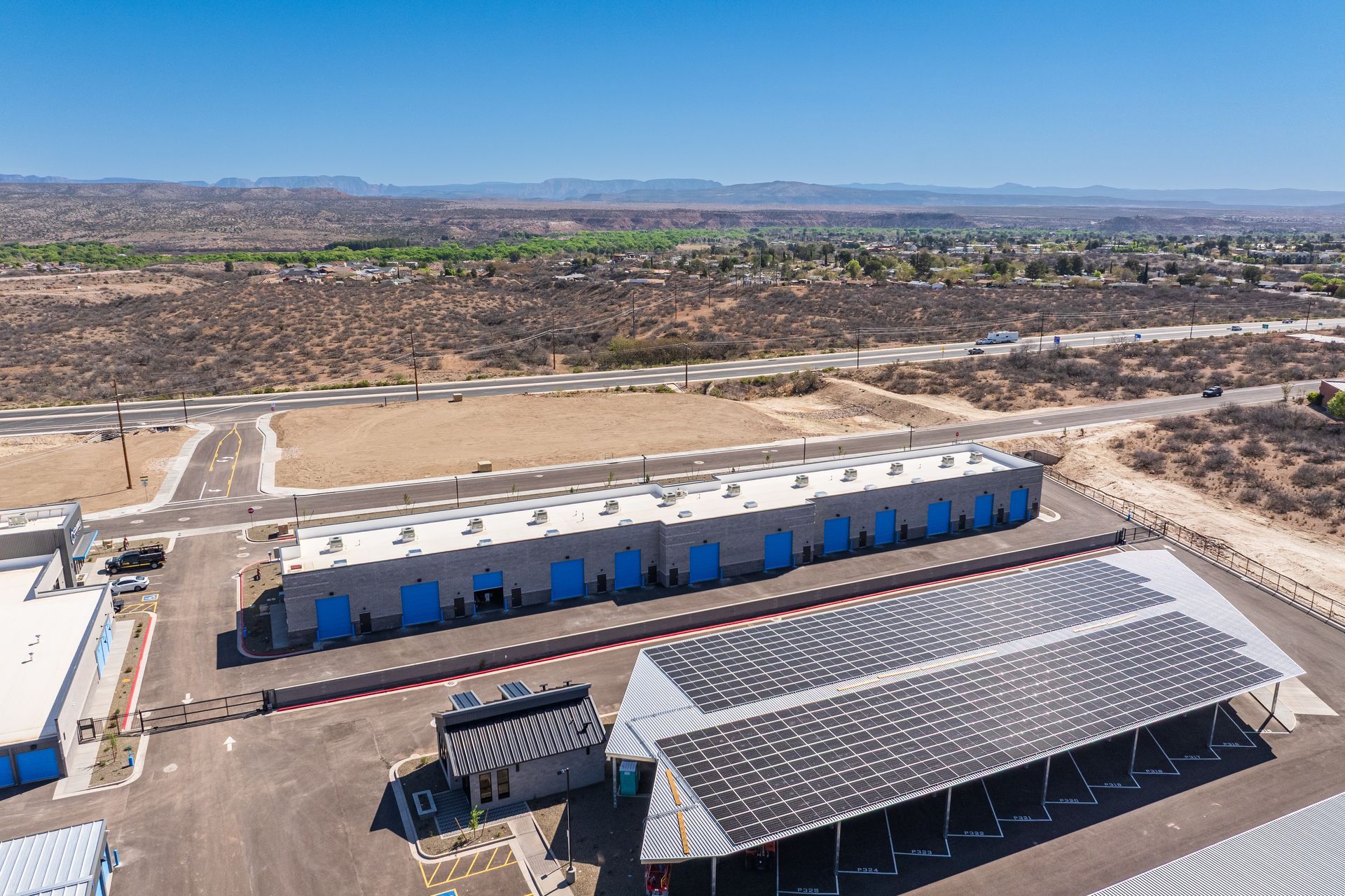 Aerial view of a storage facility with solar panels in a dry, desert-like environment with distant hills.