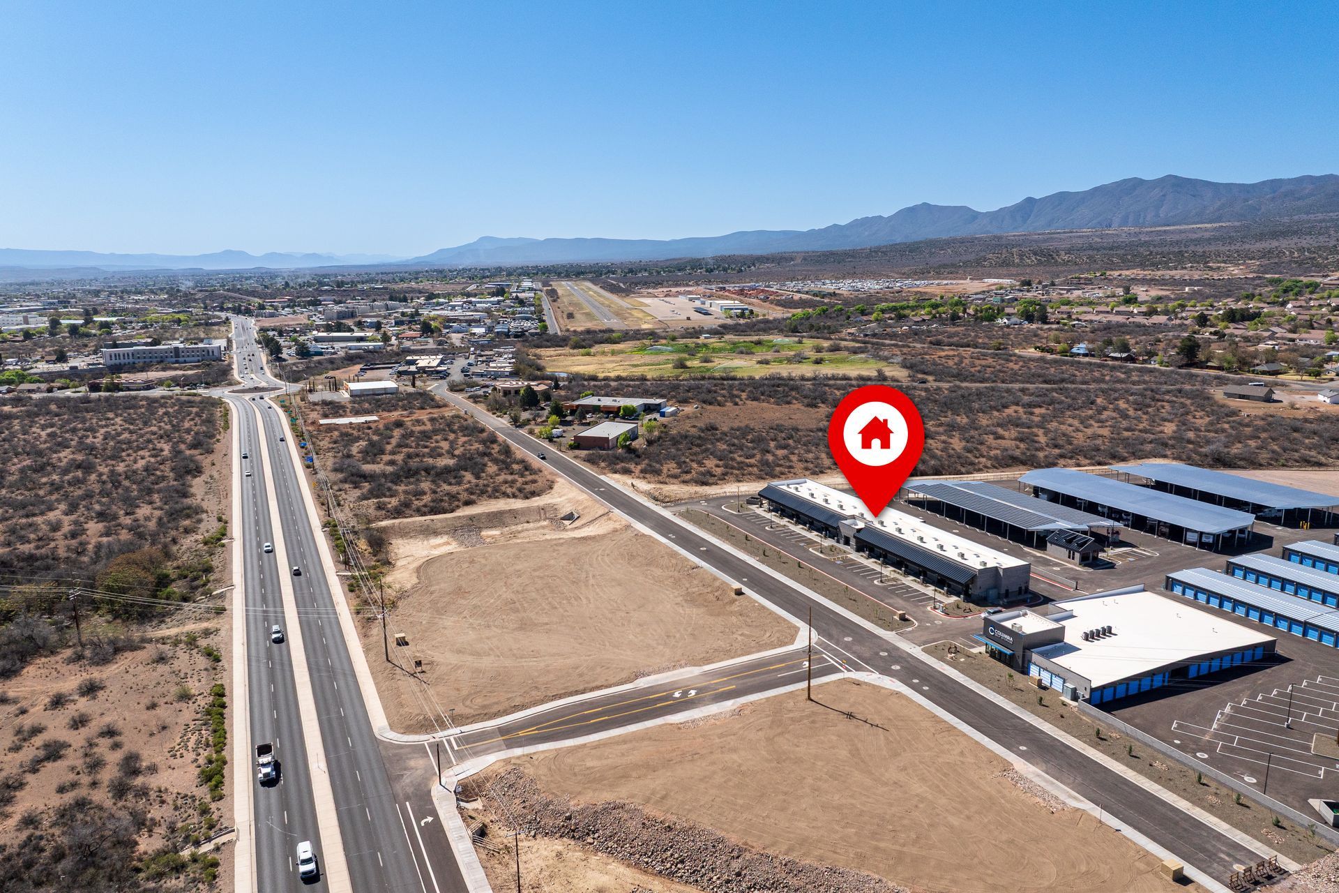 Aerial view of buildings, roads, and mountains, with a red location marker.