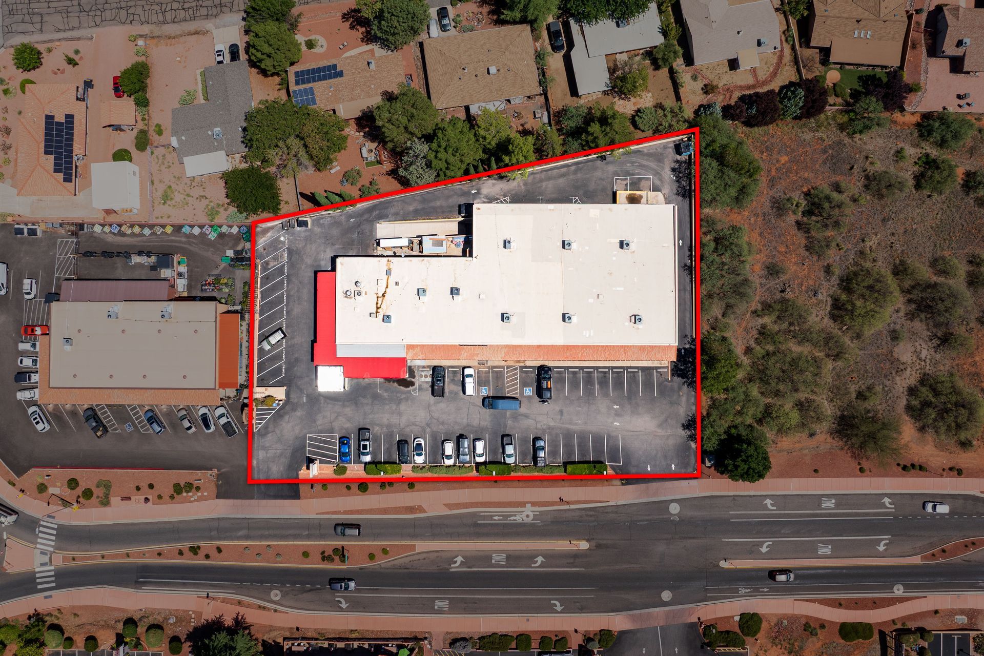 Aerial view of a commercial building with parking lot, bordered in red, alongside a road with cars.