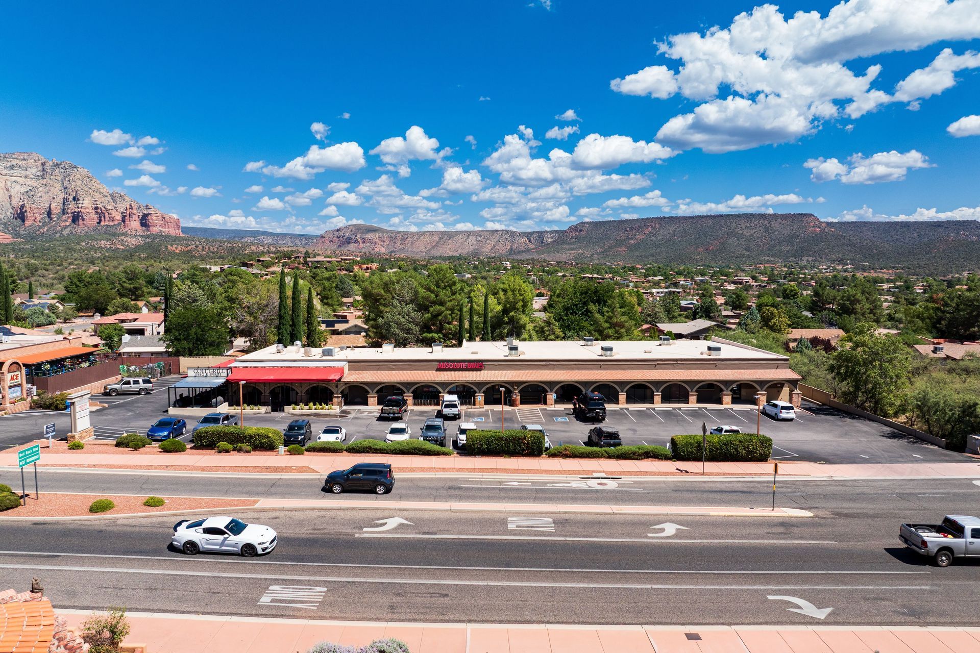 Exterior view of a commercial building with a red awning, cars, and a mountain backdrop under a blue sky.