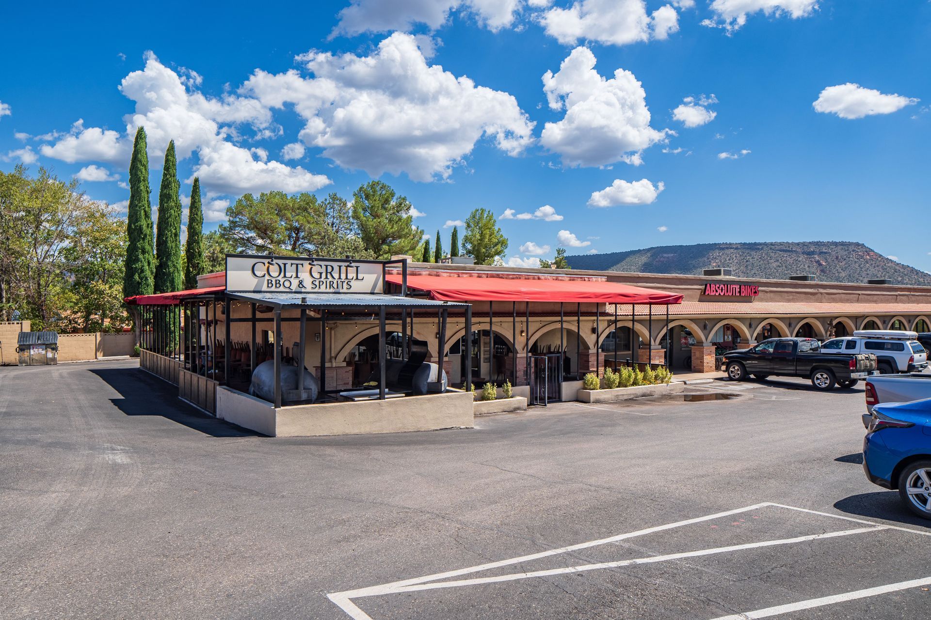Exterior of a restaurant with a red awning. Cars are parked in front. Blue sky with clouds.