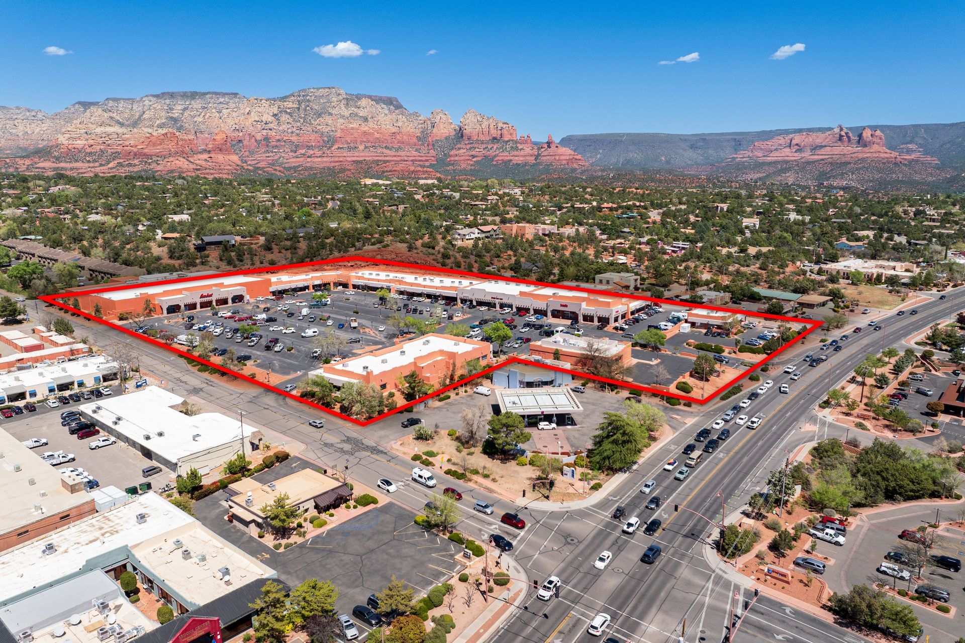 Aerial view of a commercial plaza in Sedona, Arizona, outlined in red, with red rock mountains in the background.