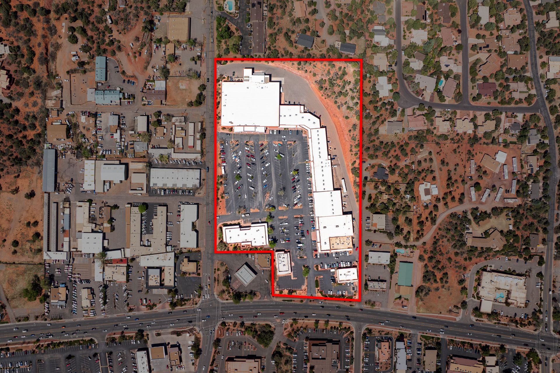 Aerial view of a commercial area, outlined in red, with buildings, parking, and surrounding roads.