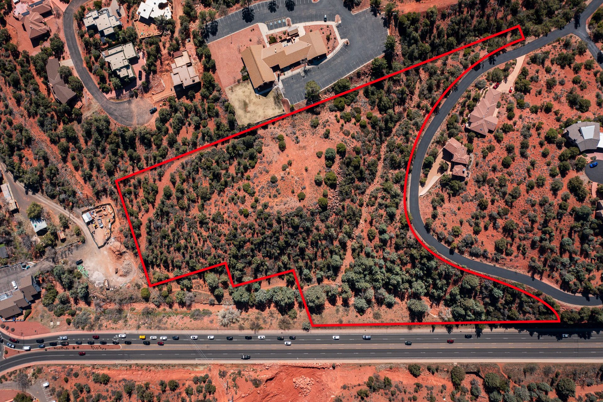 Aerial view of a plot of land outlined in red, surrounded by trees, roads, and buildings.