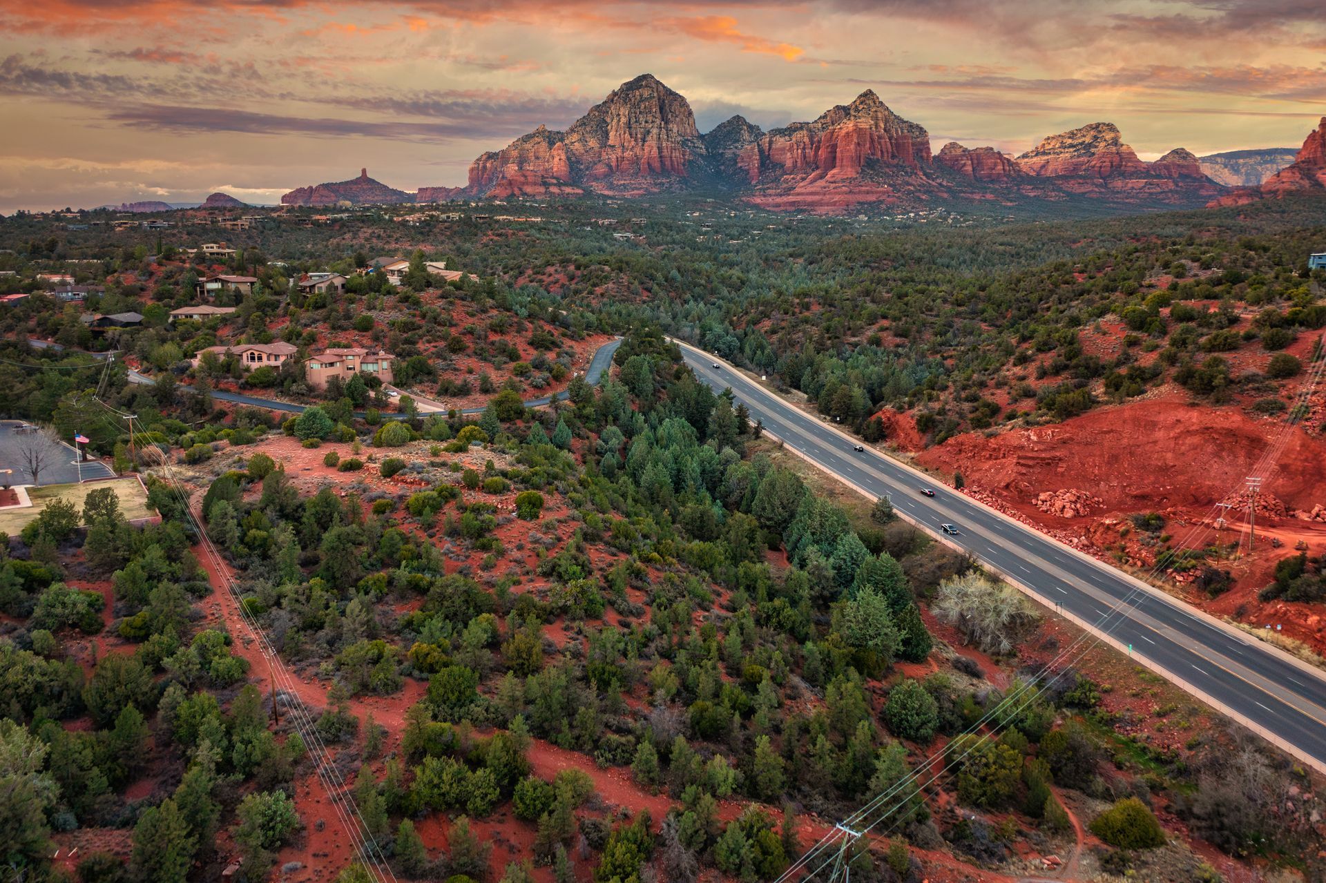 Highway through a red rock landscape, with mountains under a sunset sky.