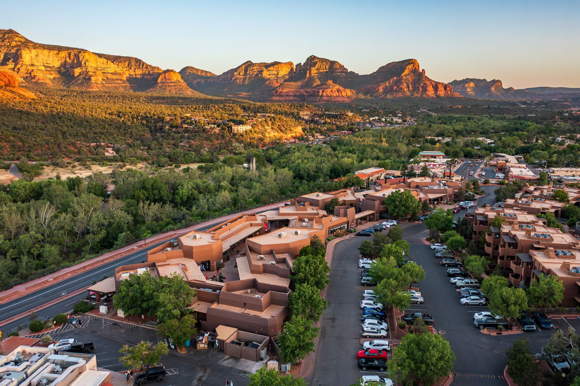 Overview of Sedona, Arizona with red rock formations at sunset. Buildings, roads, and trees in foreground.