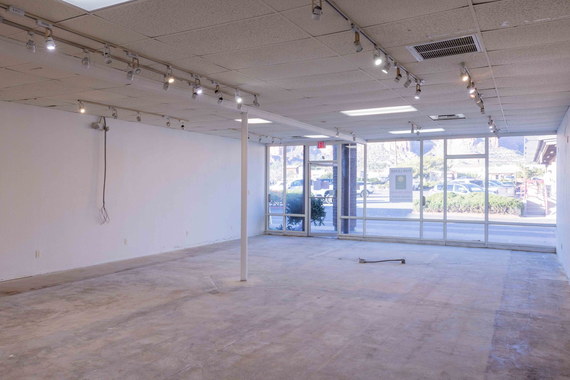 Empty, unfinished retail space with large windows facing a street. Concrete floor and white walls.