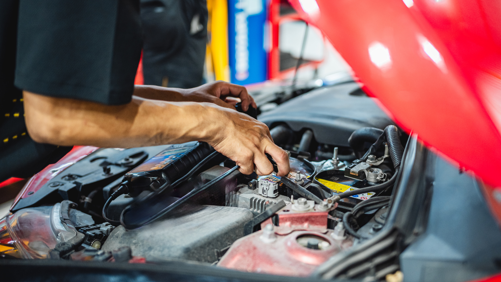 Mechanic working under an open red car hood in an auto repair shop