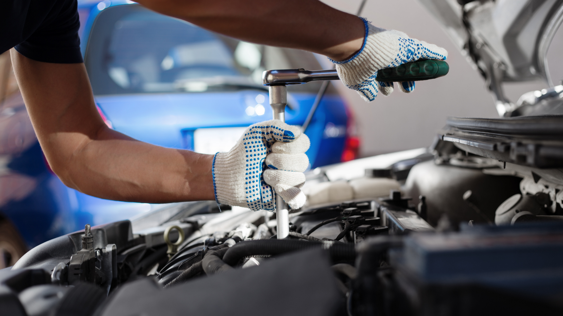 Mechanic wearing gloves inspects a car engine with a wrench in a garage.