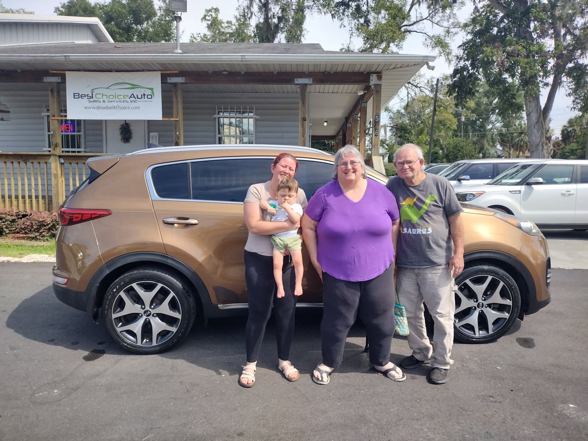 Three people standing in front of a bronze SUV outside a building.