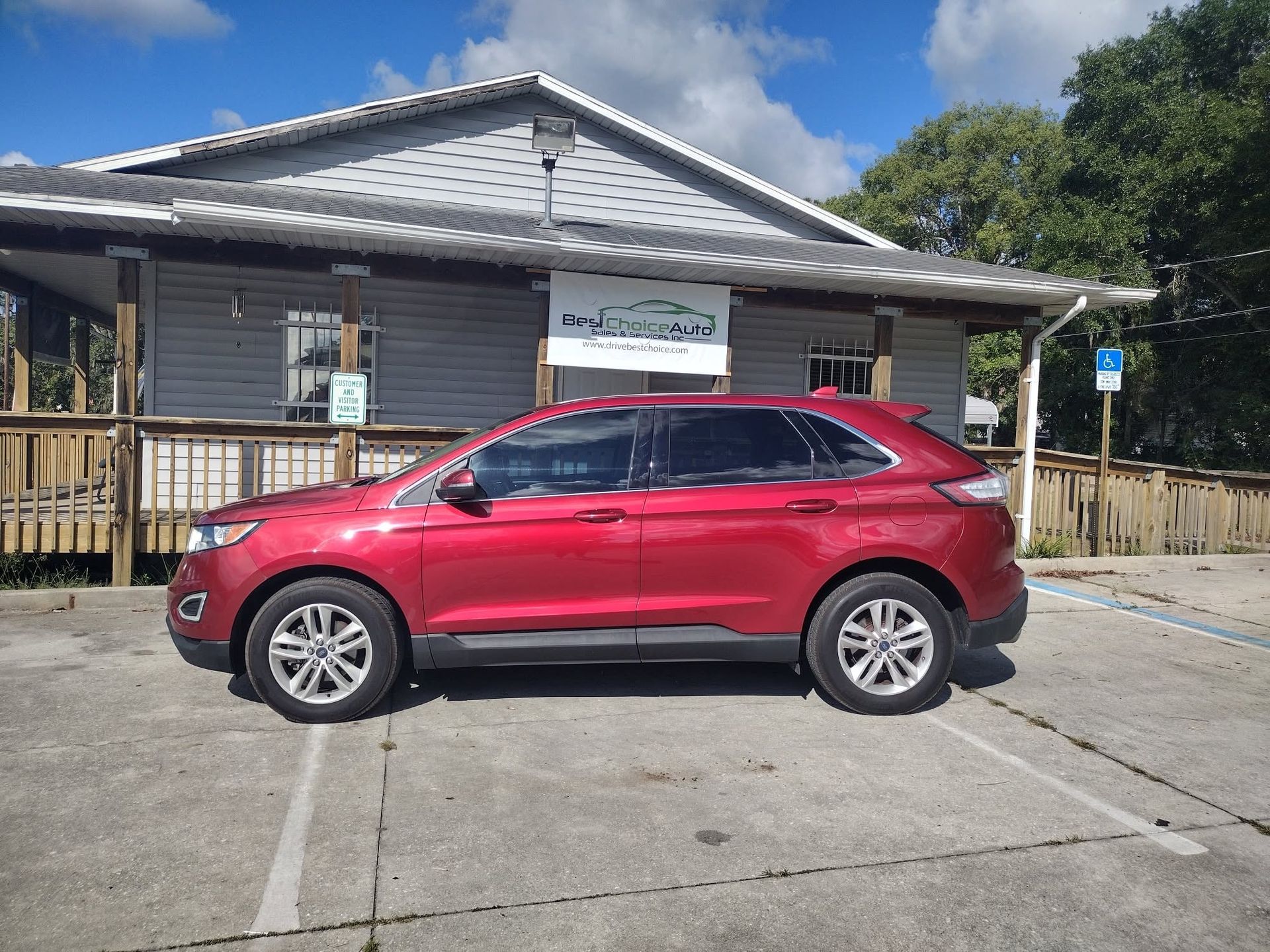 Red SUV parked in front of a small building with a porch and wooden fence.