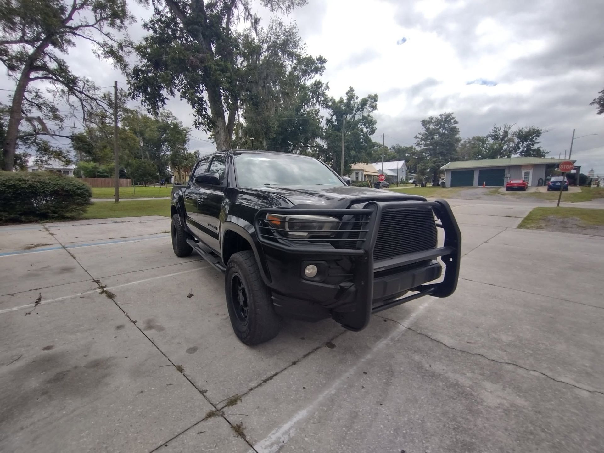 Black pickup truck with bull bar parked on a concrete lot near trees and buildings