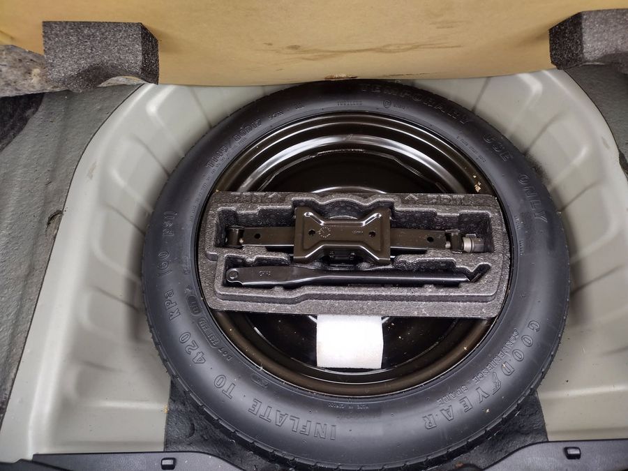 Car spare tire tucked in trunk storage compartment, seen from above.