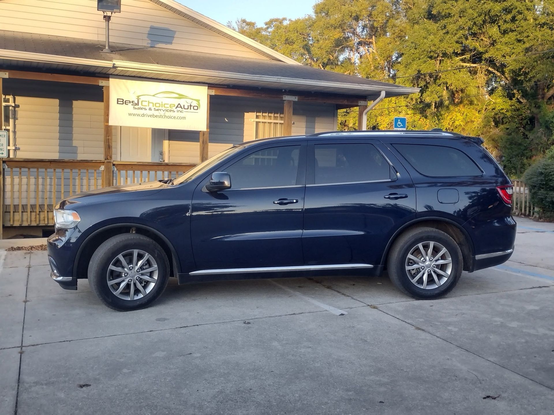 Dark blue SUV parked in front of a beige building with a porch and sign.