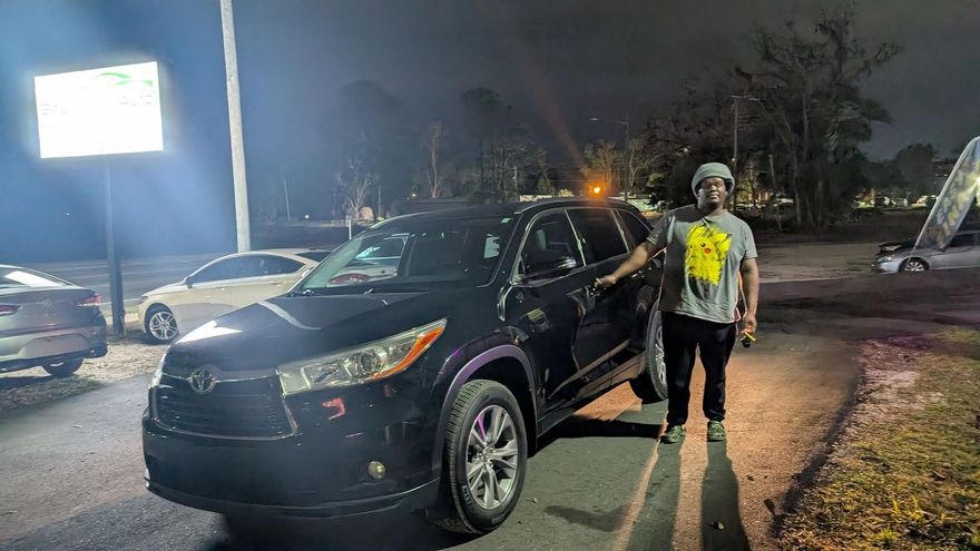 Person standing beside a black SUV in a dimly lit parking lot at night