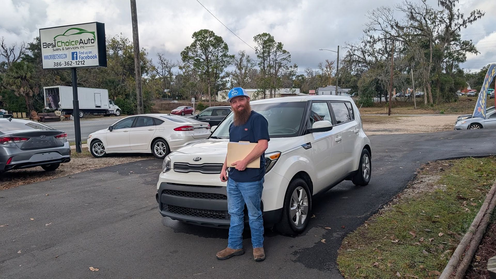 Man standing in front of a silver SUV in a parking lot, with other cars and trees nearby.