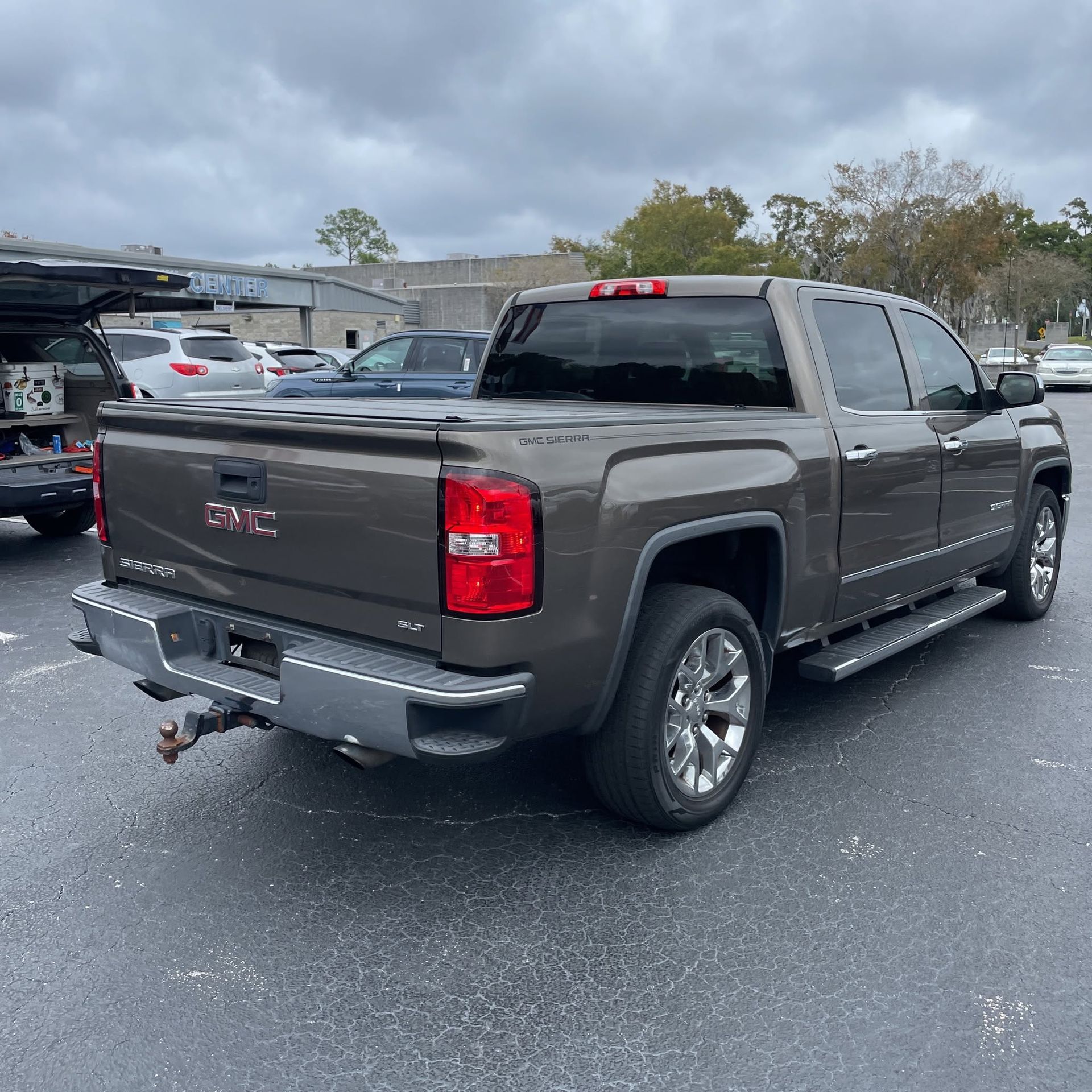 Gray GMC pickup truck parked in a lot on a wet day, rear three-quarter view