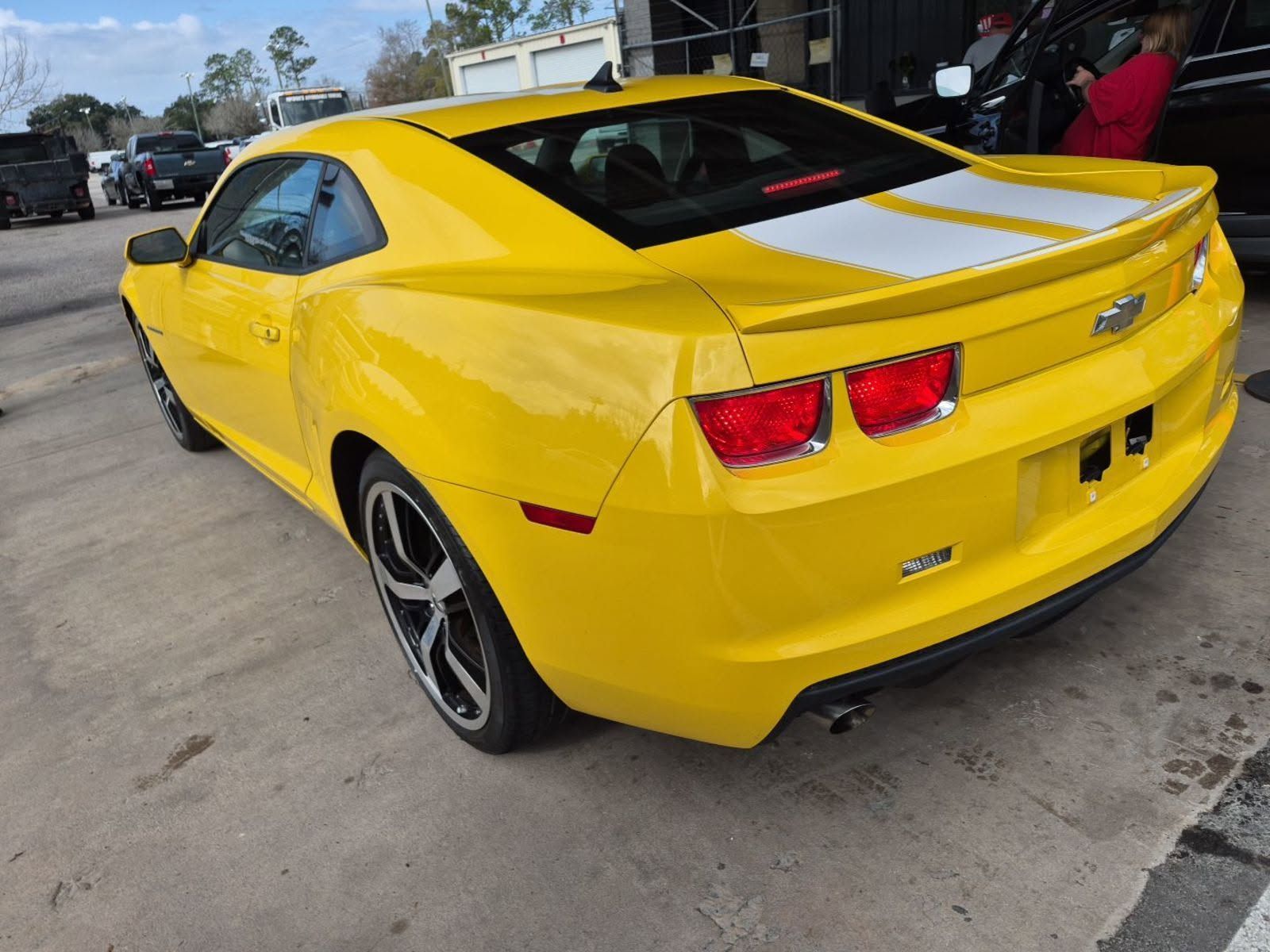Yellow Chevrolet Camaro coupe with white racing stripes, rear three-quarter view in a parking lot
