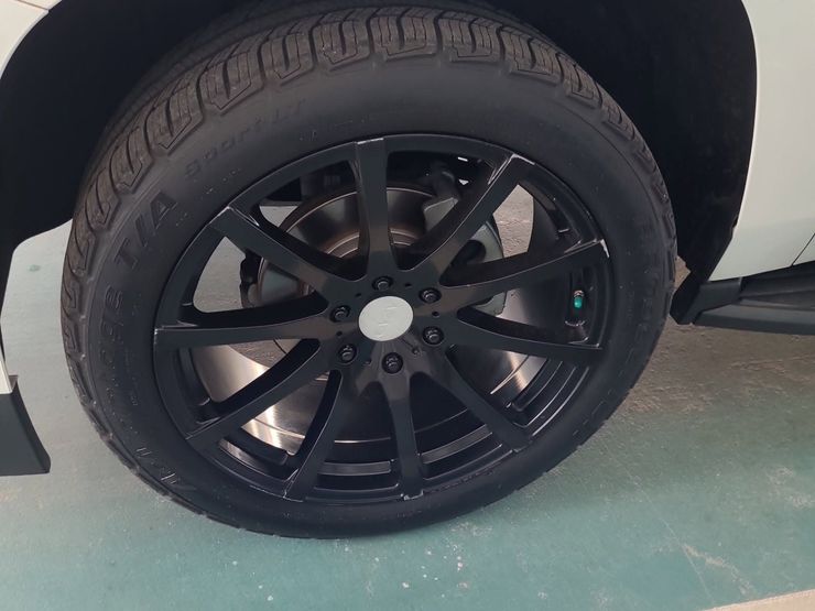 Close-up of a black car wheel with glossy black rim and tire on a light green floor.