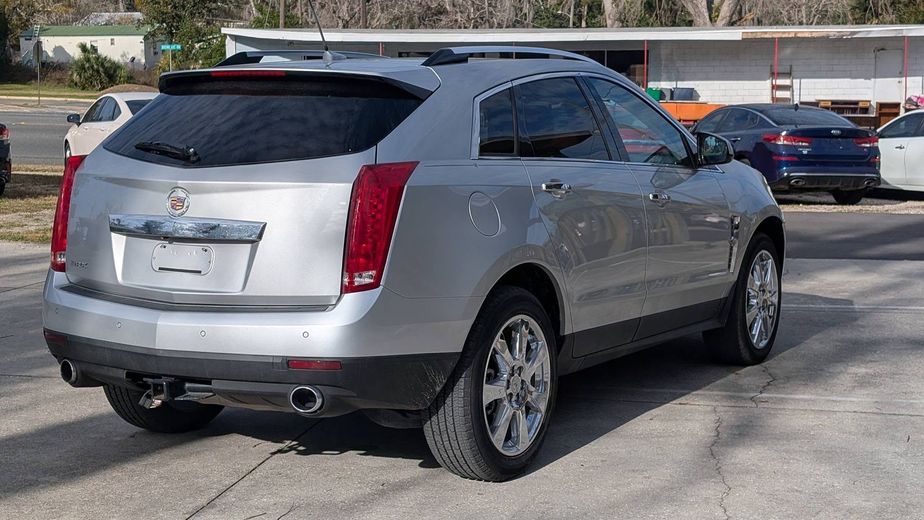 Silver Cadillac SUV parked in a lot, rear three-quarter view with tinted windows and red taillights.