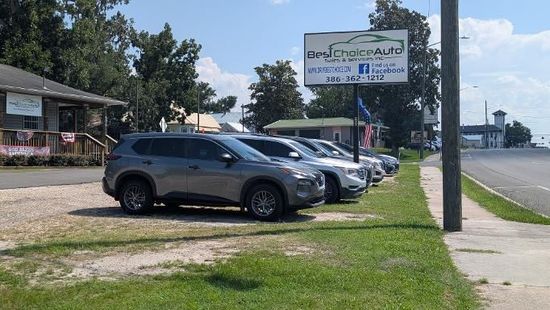 Brown pickup truck parked in a dealership lot with other vehicles and trees in the background
