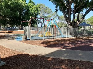 A playground with swings and a fence in a park.