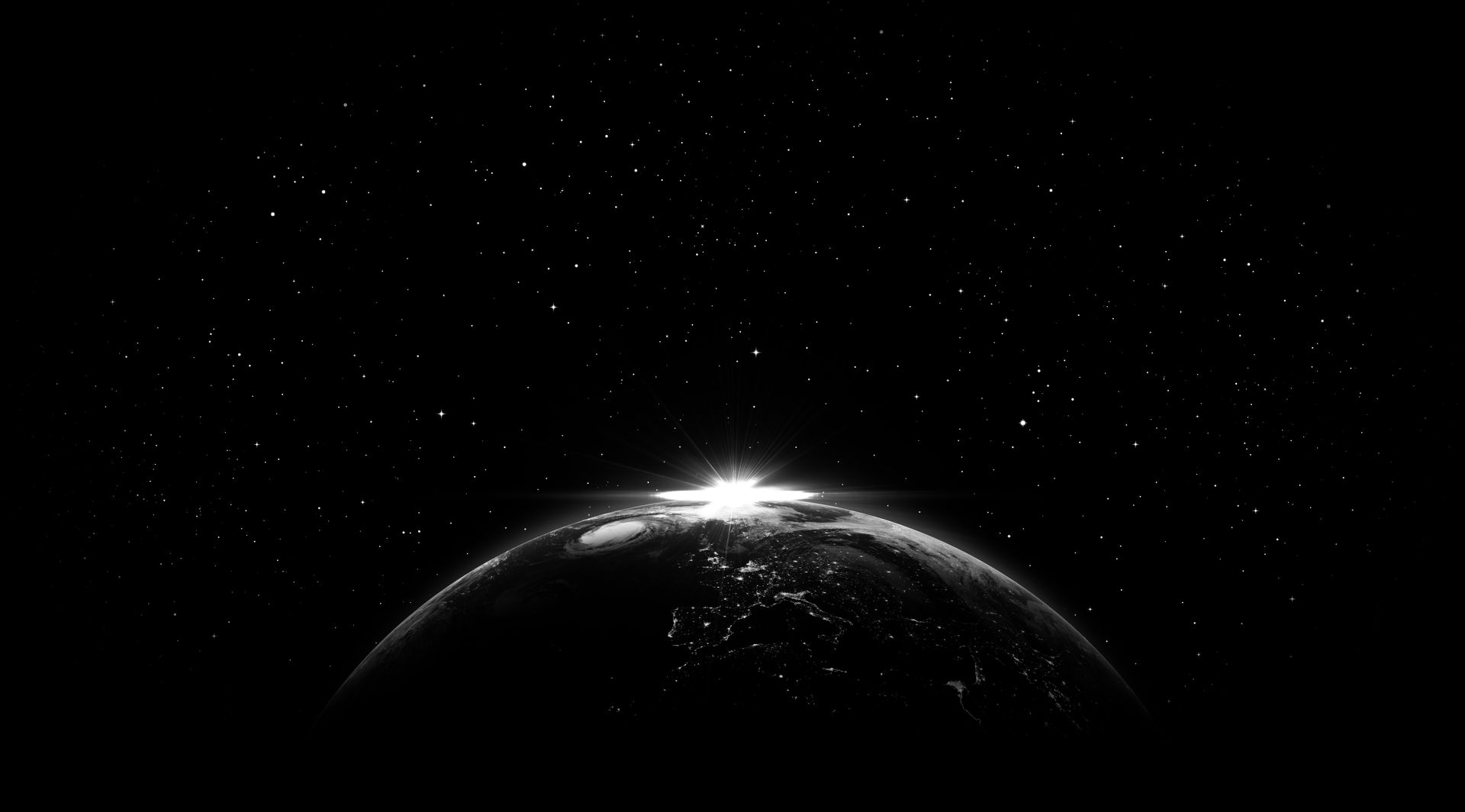 Black and white view of Earth from space with city lights illuminating the dark side. Bright light shines at the horizon.