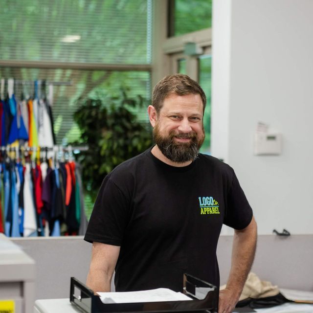 A man with a beard is wearing a black shirt that says usa apparel