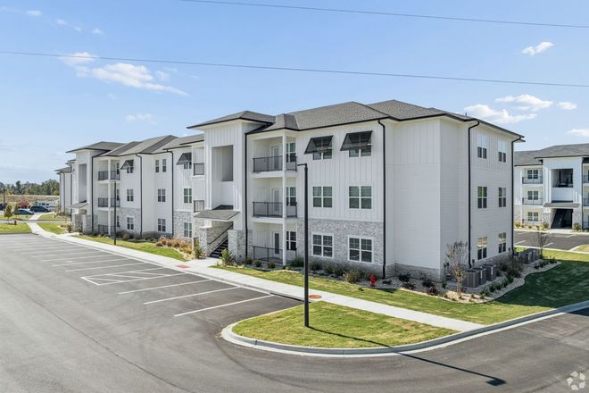 Modern white apartment buildings beside a wide paved road under a clear blue sky