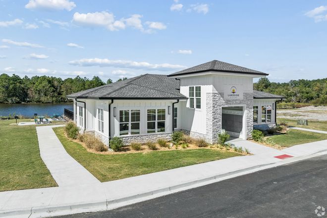 Modern single-story house with gray roof, white exterior, and landscaped yard near a lake.