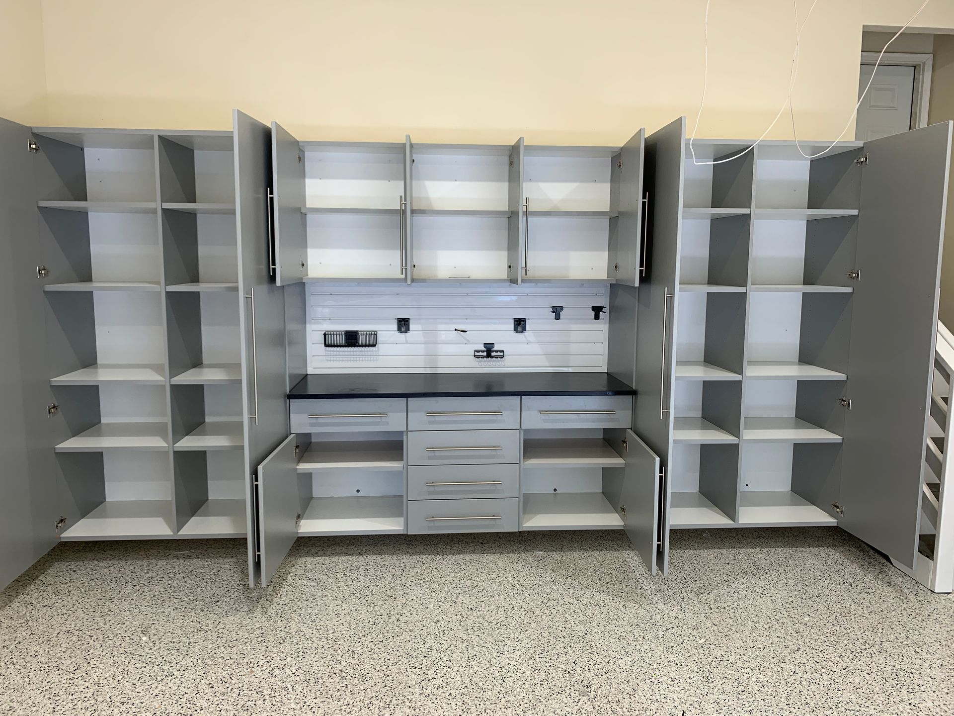 Gray built-in storage cabinets and desk with open shelves and a center workstation in an empty room