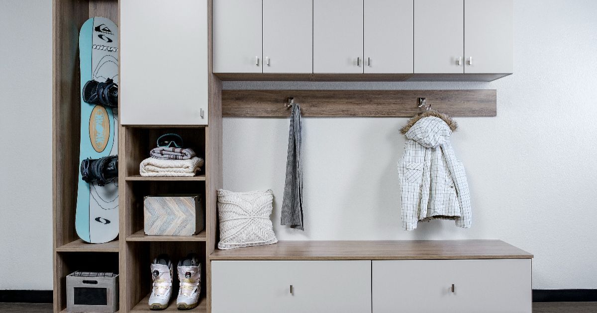 Modern white entryway bench with cabinets, shelves, and hanging coats, plus a blue snowboard on the left.